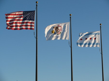 U.S., Illinois and City of Chicago flags in a stiff breeze at the Navy Pier, Chicago. Photo by John Junker, at flickr.